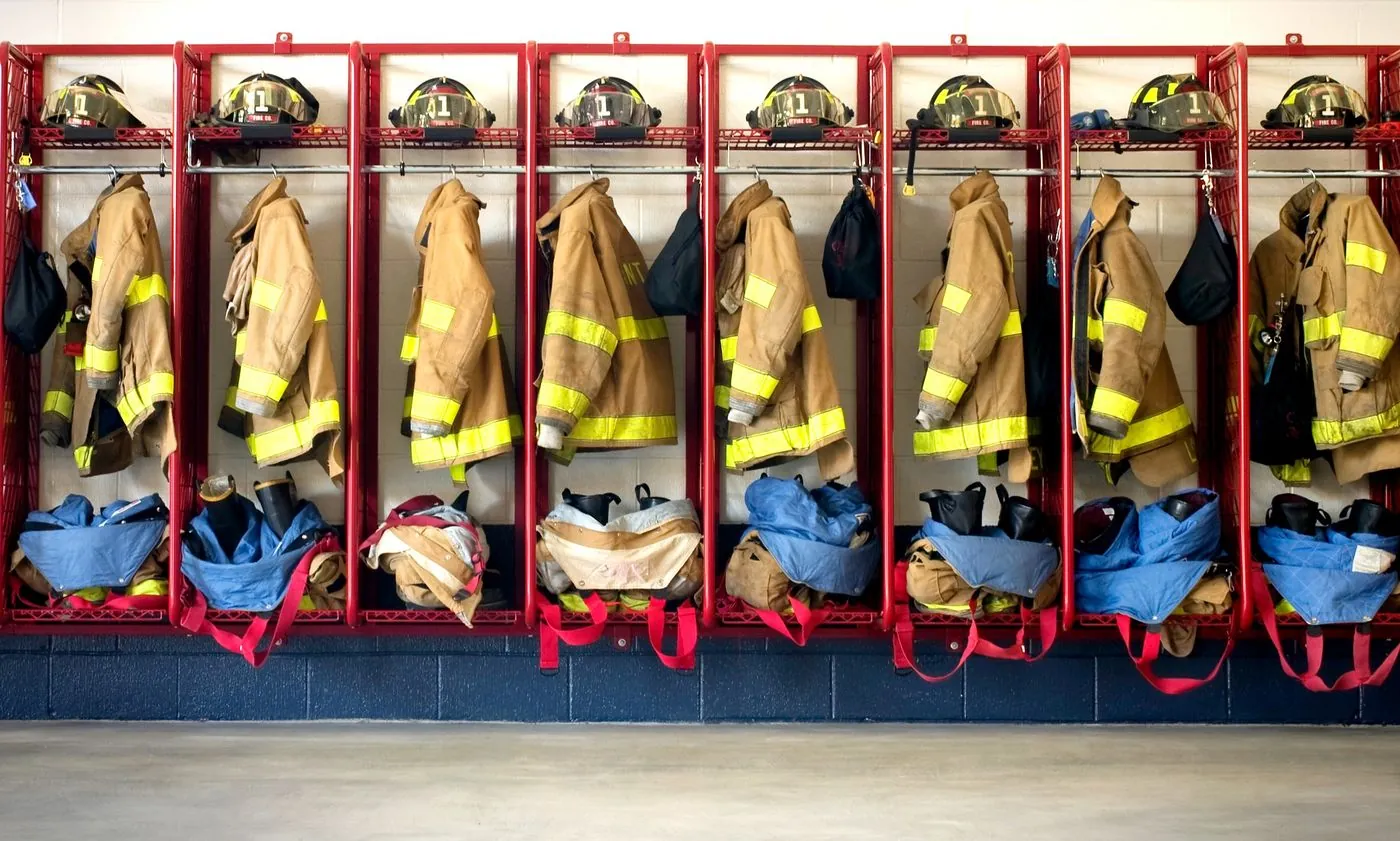 Roupas e capacetes de proteção de bombeiros organizados lado a lado em armários vermelhos.